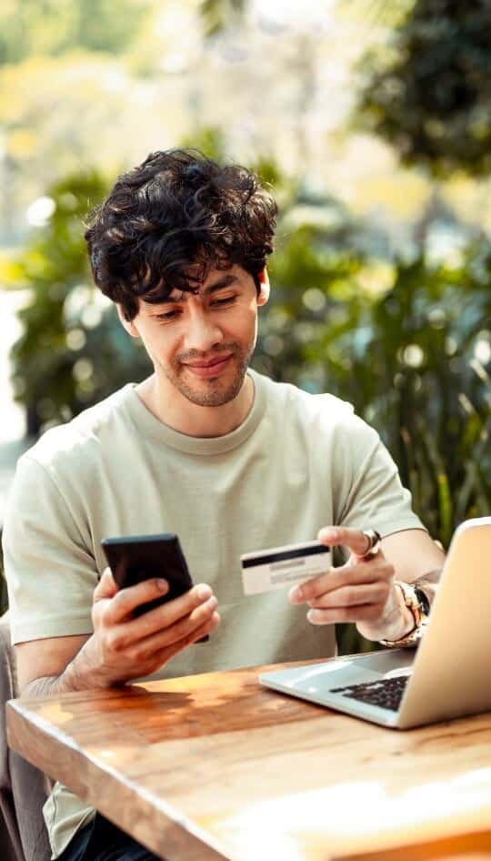 Man sitting outside holding a credit card and using his smartphone