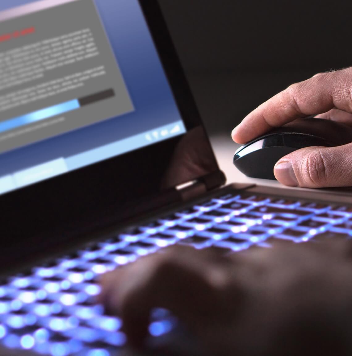 Persons hands typing on a laptop and using a mouse