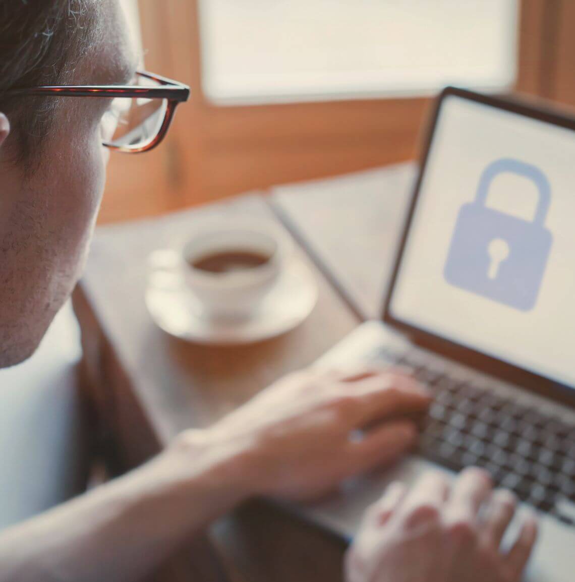 Man having coffee working on a laptop with a padlock on the screen