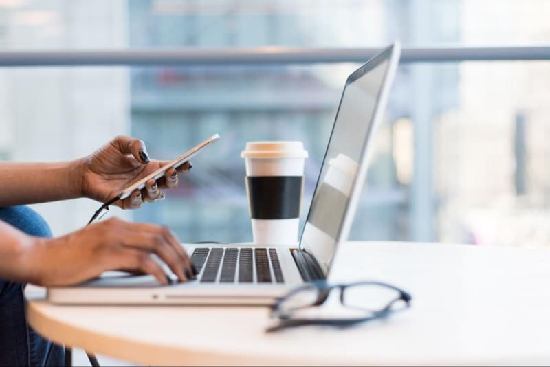 Woman at work holding an iPhone while working on a laptop