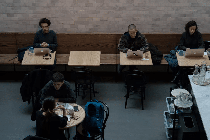 Multiple people working on laptops in a public cafe